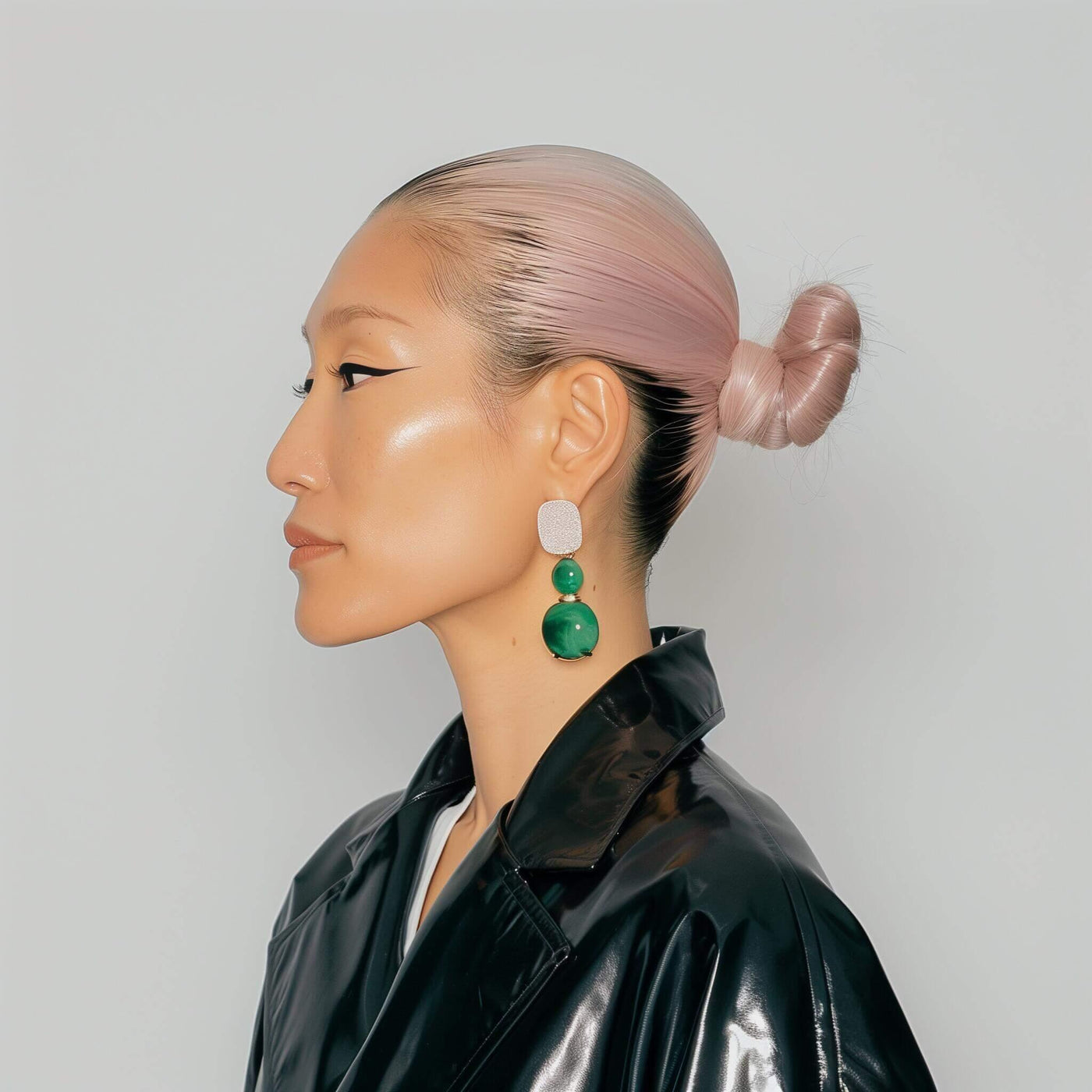 Profile of woman with pink hair bun, bold eyeliner, green statement earrings, and black leather jacket