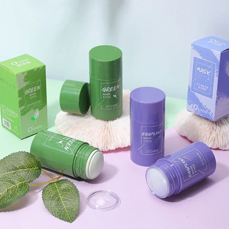 Green and purple O'Cheal mask sticks with matching boxes on pastel background with green leaves and white brush