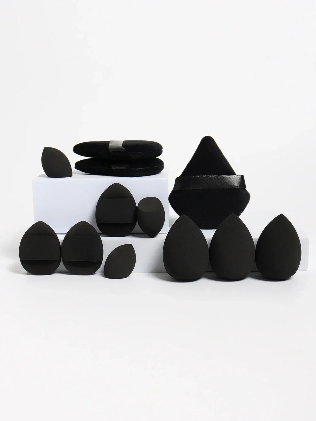 Various black makeup sponges and applicators in teardrop and triangular shapes on white blocks