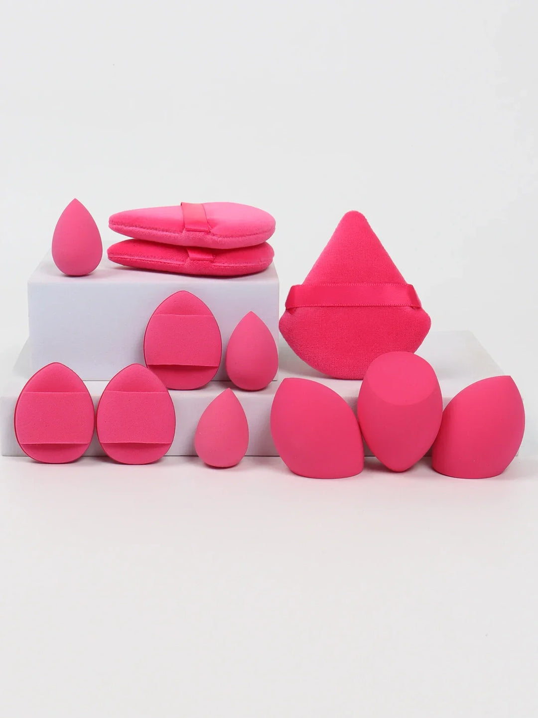Various bright pink makeup sponges and applicator puffs on white blocks
