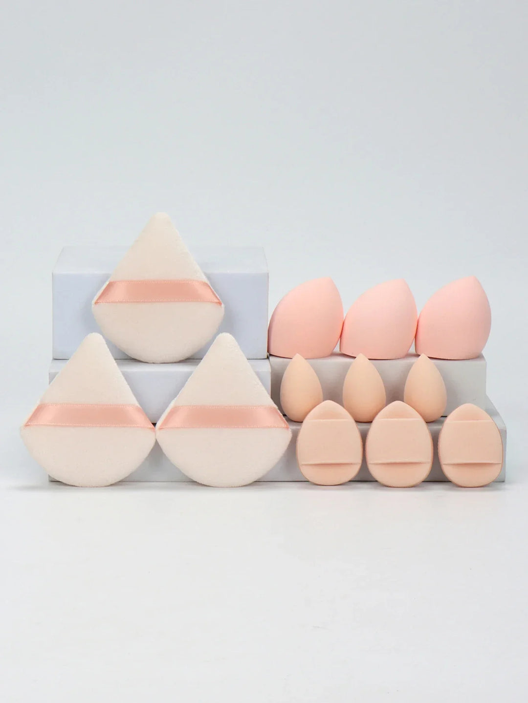 Set of various soft makeup sponges and powder puffs in light peach tones arranged on white blocks