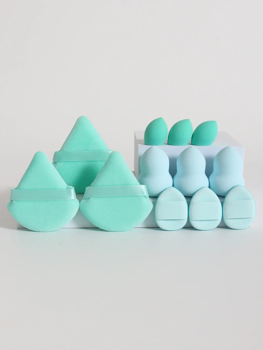 Various makeup sponges and puffs in blue and mint green shades on white background