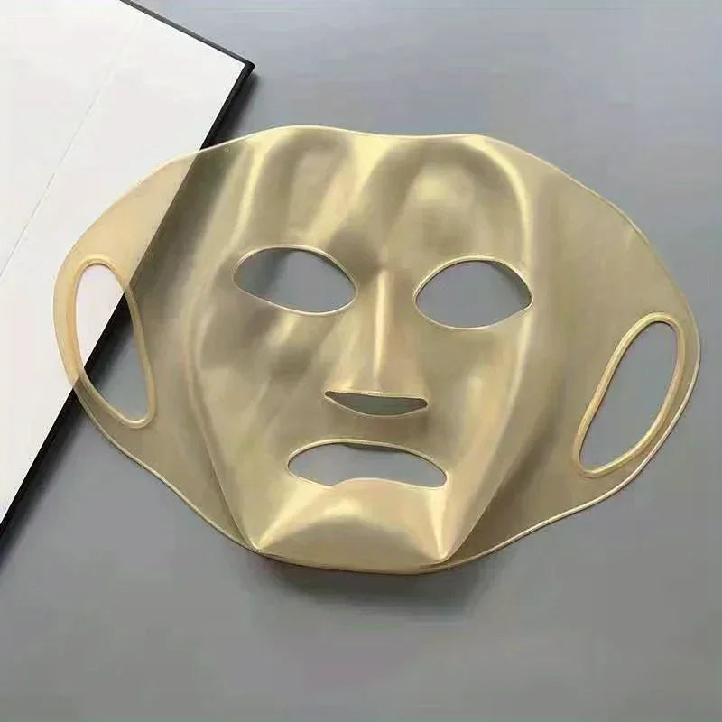 Gold-colored facial mask with cutouts for eyes, nose, and mouth on gray surface