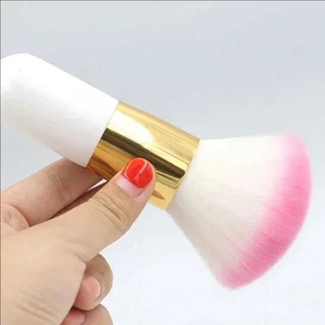 Hand holding soft makeup brush with white handle, gold ferrule, and white bristles tipped in pink
