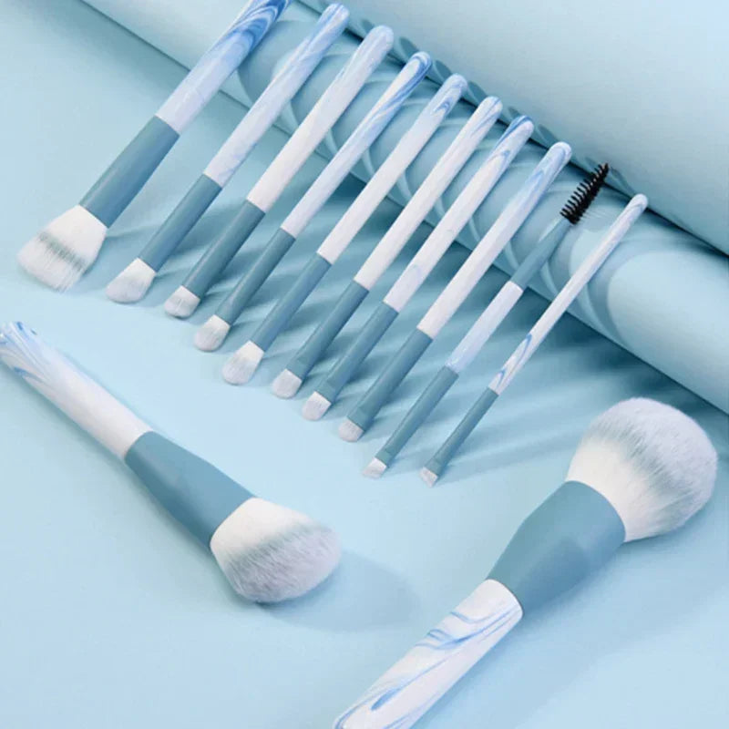 Set of blue and white marble makeup brushes on light blue background, various brush types included