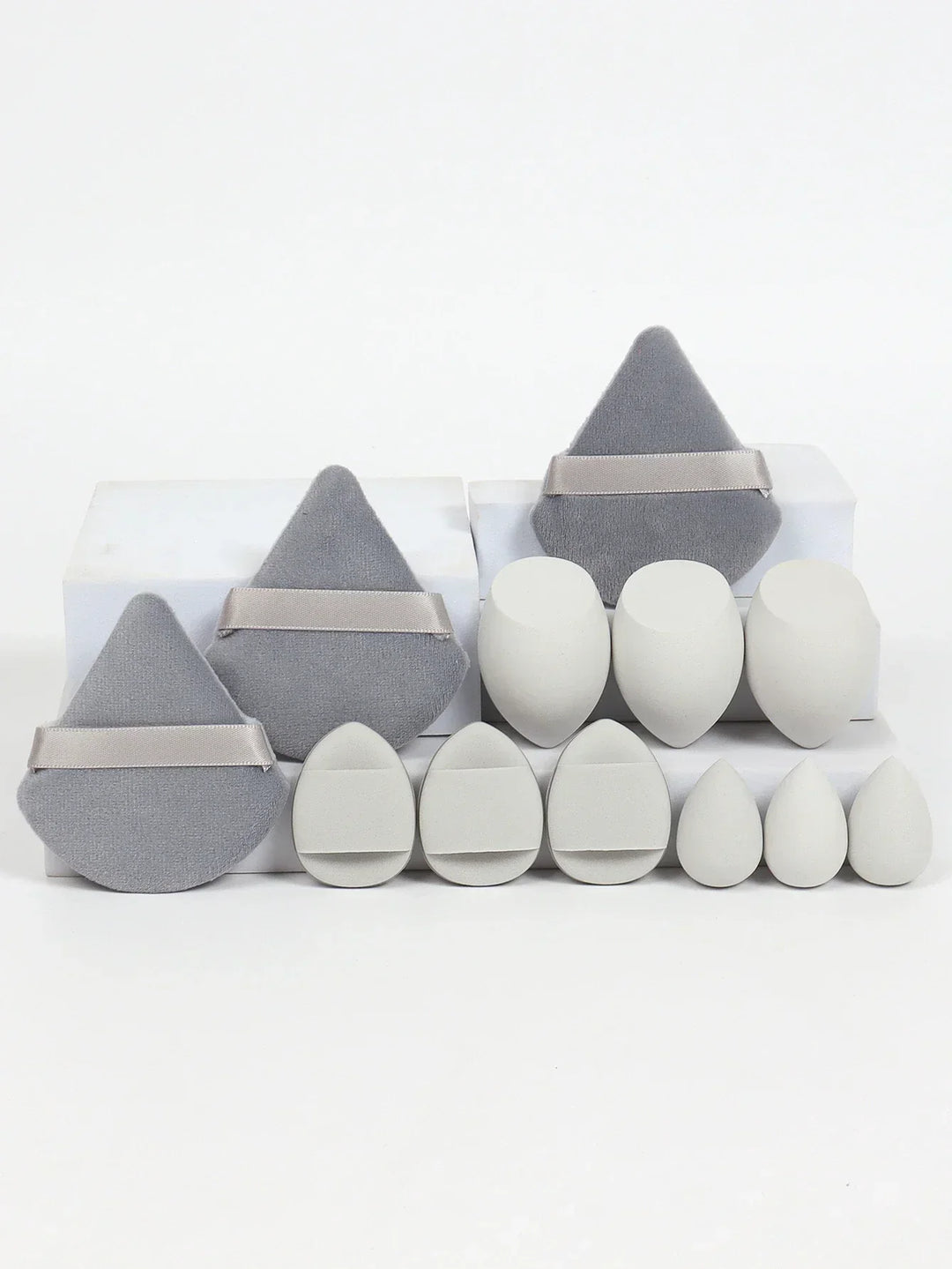 Set of white makeup sponges and grey powder puffs in various shapes on white blocks