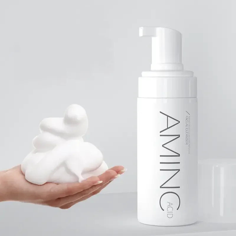 White bottle of amino acid facial cleanser with foam on hand against light background