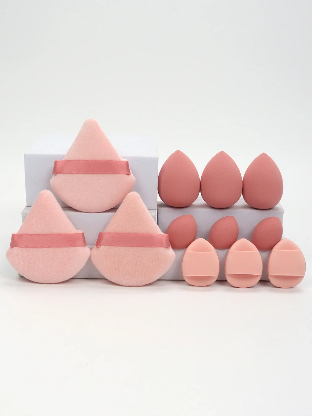 Various pink makeup sponges and powder puffs in different shapes and sizes organized on white blocks
