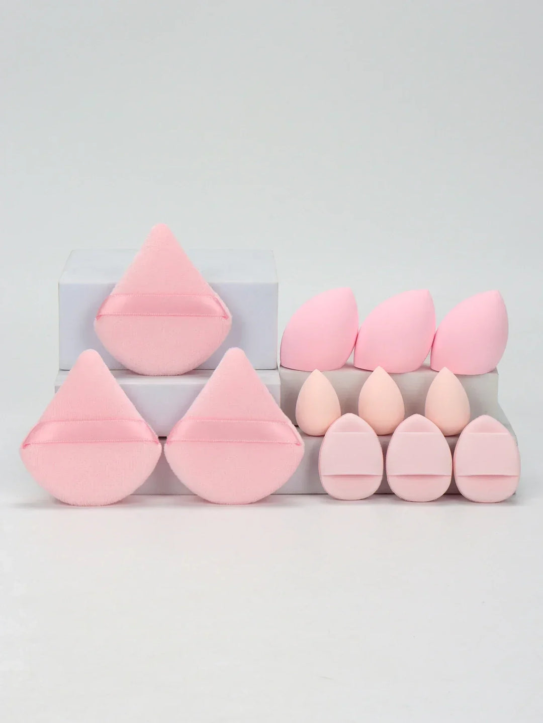 Set of pink makeup sponges and powder puffs in various shapes arranged on white blocks