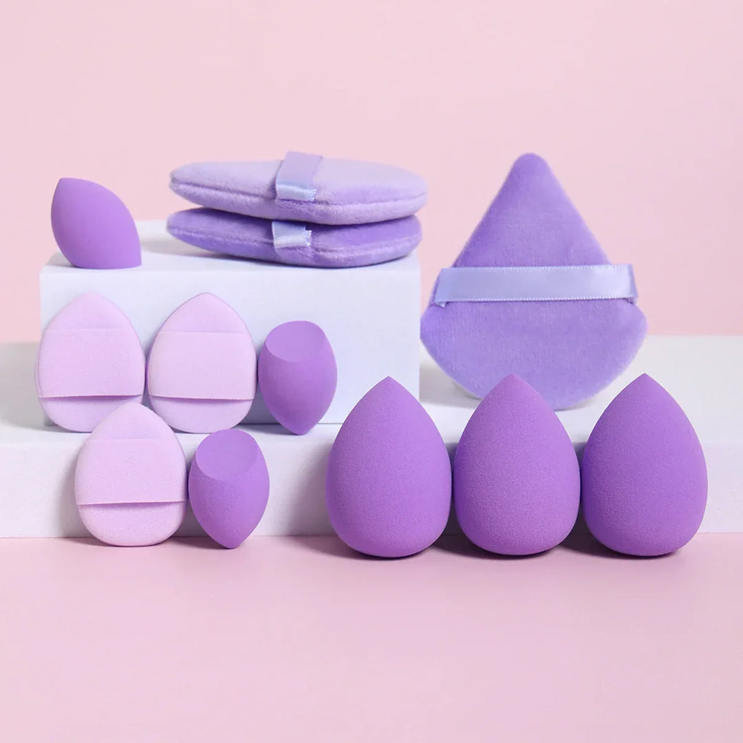 Various purple and lavender makeup sponges and powder puffs on white blocks with a pink background