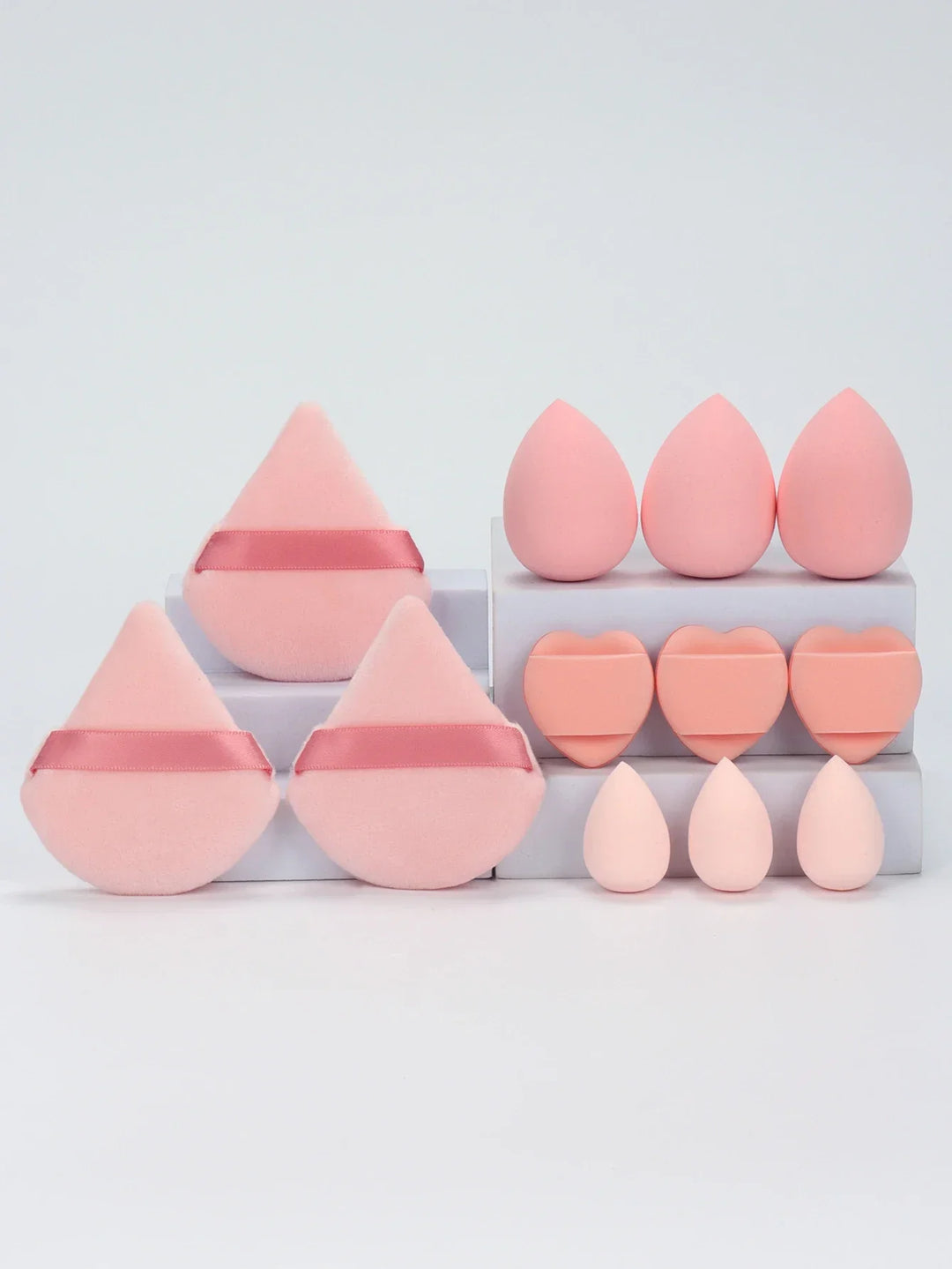Set of pink makeup sponges and powder puffs on white blocks, various shapes including teardrop and heart