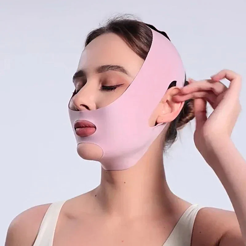 Woman wearing a pink facial slimming mask with cutouts for eyes, mouth, and chin against a plain background