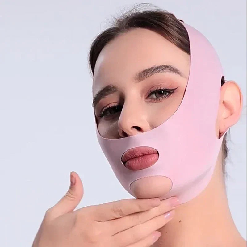 Woman wearing pink facial slimming mask with cutouts on chin and mouth against light background