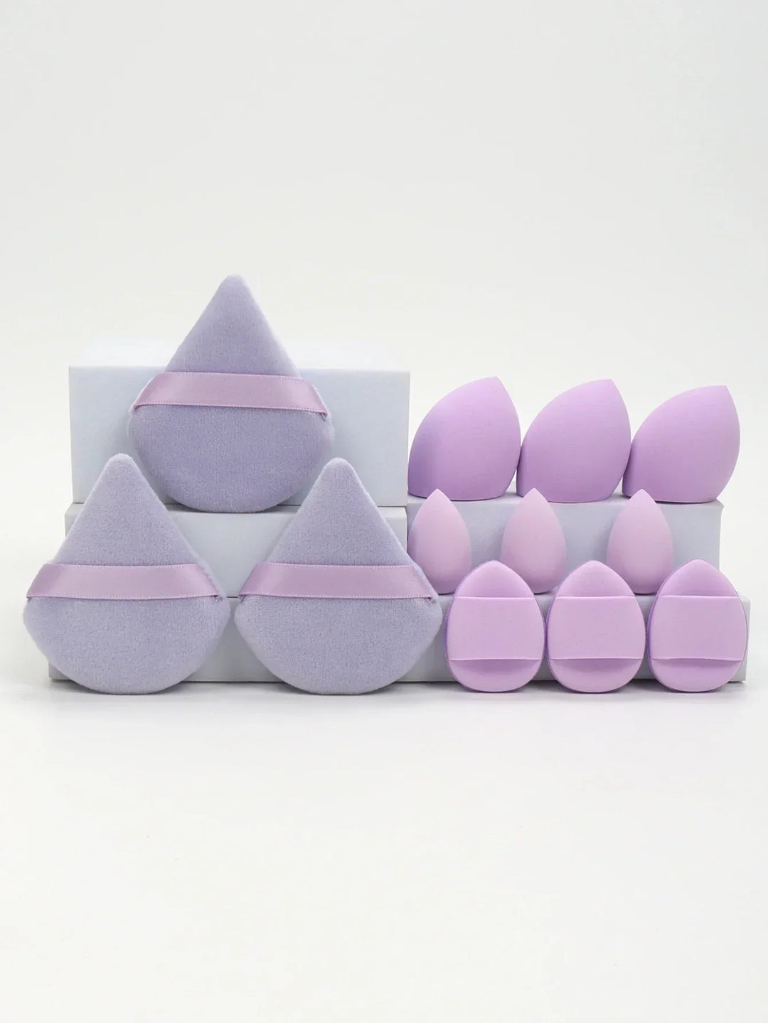 Various purple makeup sponges and powder puffs arranged on white blocks, different shapes and sizes