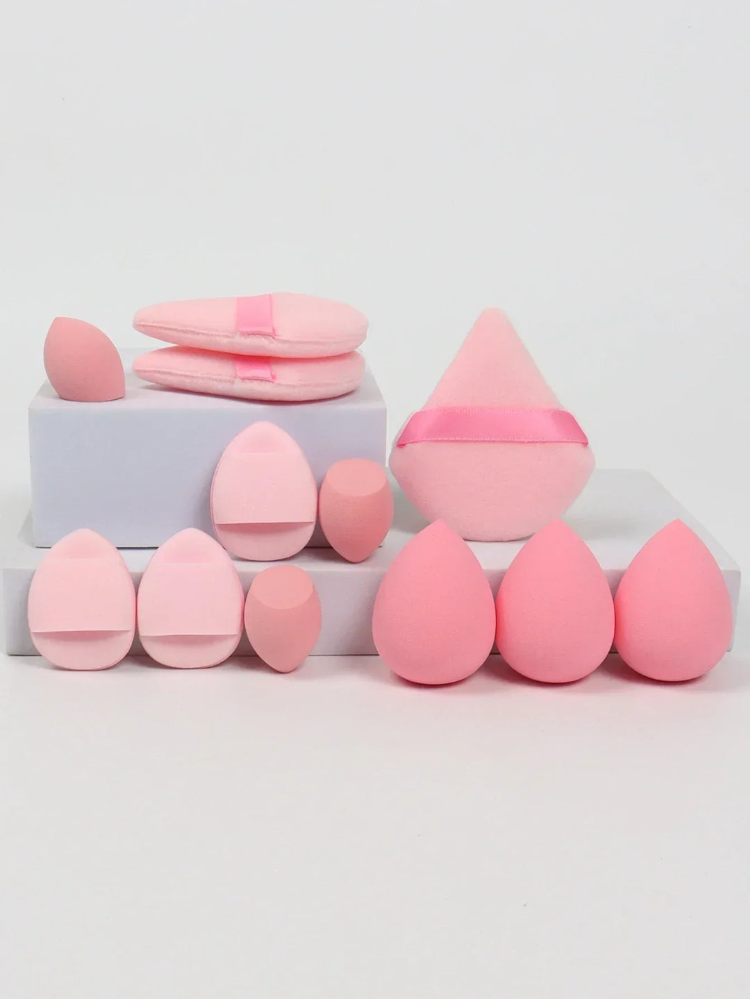 Set of various pink makeup sponges and applicators on white blocks, including teardrop and triangular shapes