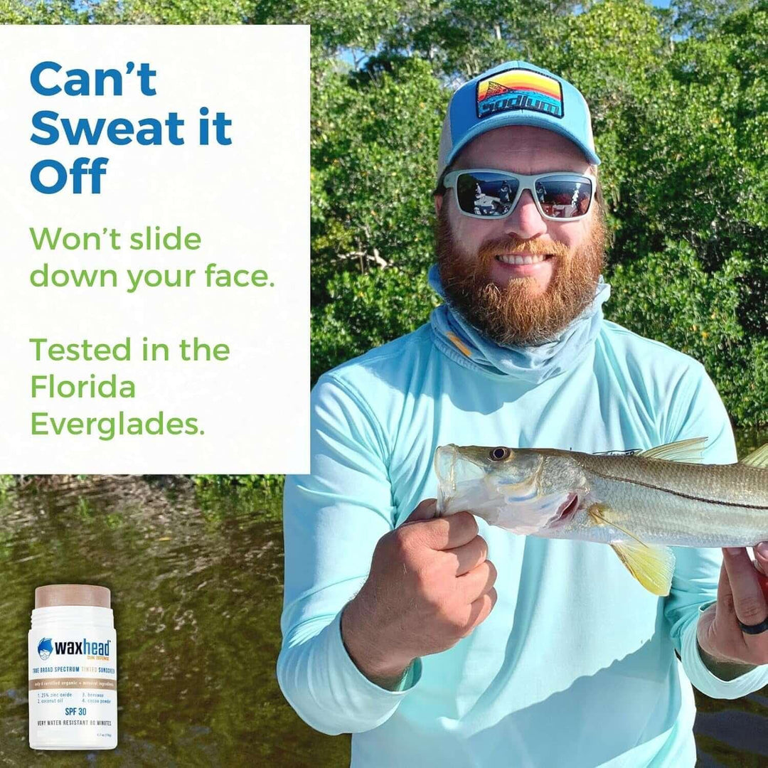 Man in sunglasses and hat holding fish in Florida Everglades, promoting sweat-resistant Waxhead sunscreen